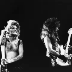 Ozzy Osbourne z mikrofonem i gitarzysta na scenie. Ikoniczny wokalista, znany z kontrowersyjnych występów, niczym ozzy osbourne bat, w swoim żywiole.
