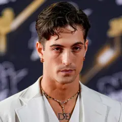 Damiano David w białej marynarce, z naszyjnikiem i kolczykami, gotowy na koncert.