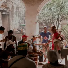 Ludzie w Guantanamera, w tym mężczyzna w czerwonym stroju i kapeluszu, ściskają sobie dłonie.