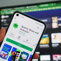 Dłoń trzyma smartfon z ekranem sklepu Google Play, gdzie widoczna jest strona aplikacji Spotify. To świetna okazja, by skorzystać z **spotify promocja** i pobrać ulubioną muzykę i podcasty.