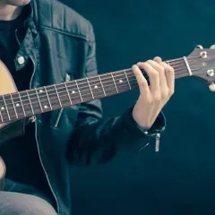 Dłoń gitarzysty na gryfie gitary akustycznej, grającego akord.