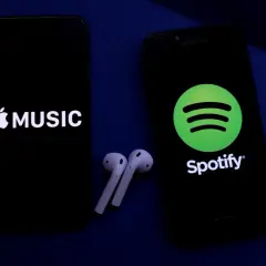 Dwa telefony z logotypami Apple Music i Spotify, obok słuchawki bezprzewodowe. Wybór najlepszych platform streamingowych.