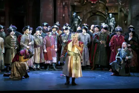 Aktorzy w historycznych strojach na scenie. W centrum mężczyzna w bogatym stroju, gestykuluje. To z pewnością będzie przebój!
