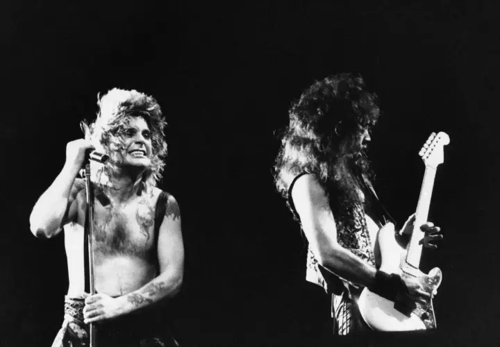Ozzy Osbourne z mikrofonem i gitarzysta na scenie. Ikoniczny wokalista, znany z kontrowersyjnych występów, niczym ozzy osbourne bat, w swoim żywiole.