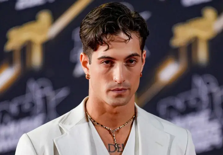 Damiano David w białej marynarce, z naszyjnikiem i kolczykami, gotowy na koncert.