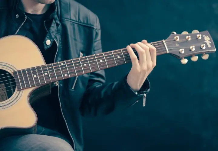 Dłoń gitarzysty na gryfie gitary akustycznej, grającego akord.