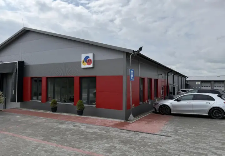 Nowoczesny budynek z czerwonymi akcentami i logo "PIRAT". Obok zaparkowane samochody, jeden srebrny, który wygląda jak z salonu, a nie jak bootleg.