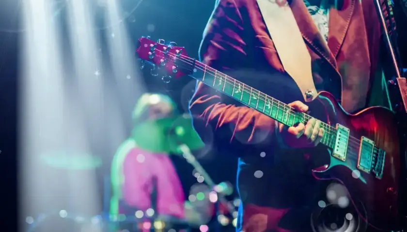 Koncertowy gitarzysta grający na scenie, przypominający klimatem piosenki lat 90. W tle perkusista.