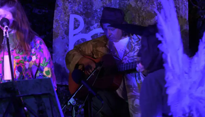 Muzyk gra na gitarze, a wokalistka śpiewa. Atmosfera sugeruje starorzymską pieśń żałobną.