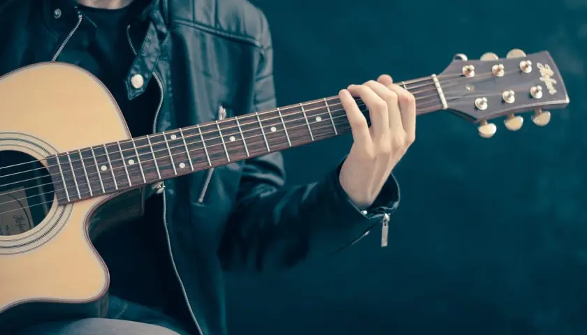 Dłoń gitarzysty na gryfie gitary akustycznej, grającego akord.