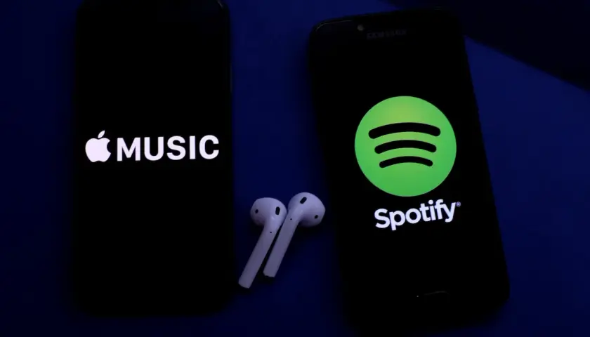 Dwa telefony z logotypami Apple Music i Spotify, obok słuchawki bezprzewodowe. Wybór najlepszych platform streamingowych.