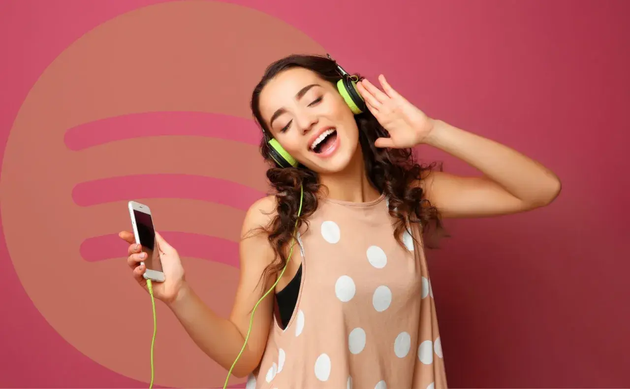 Dziewczyna z słuchawkami na uszach i telefonem w dłoni, ciesząca się muzyką. Idealna okazja, by sprawdzić Spotify Premium za 0,99!