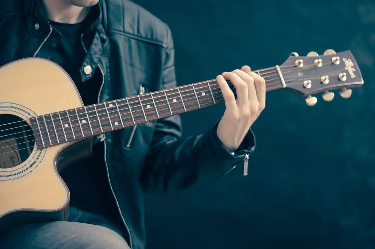 Dłoń gitarzysty na gryfie gitary akustycznej, grającego akord.