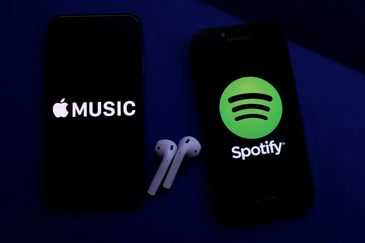 Dwa telefony z logotypami Apple Music i Spotify, obok słuchawki bezprzewodowe. Wybór najlepszych platform streamingowych.