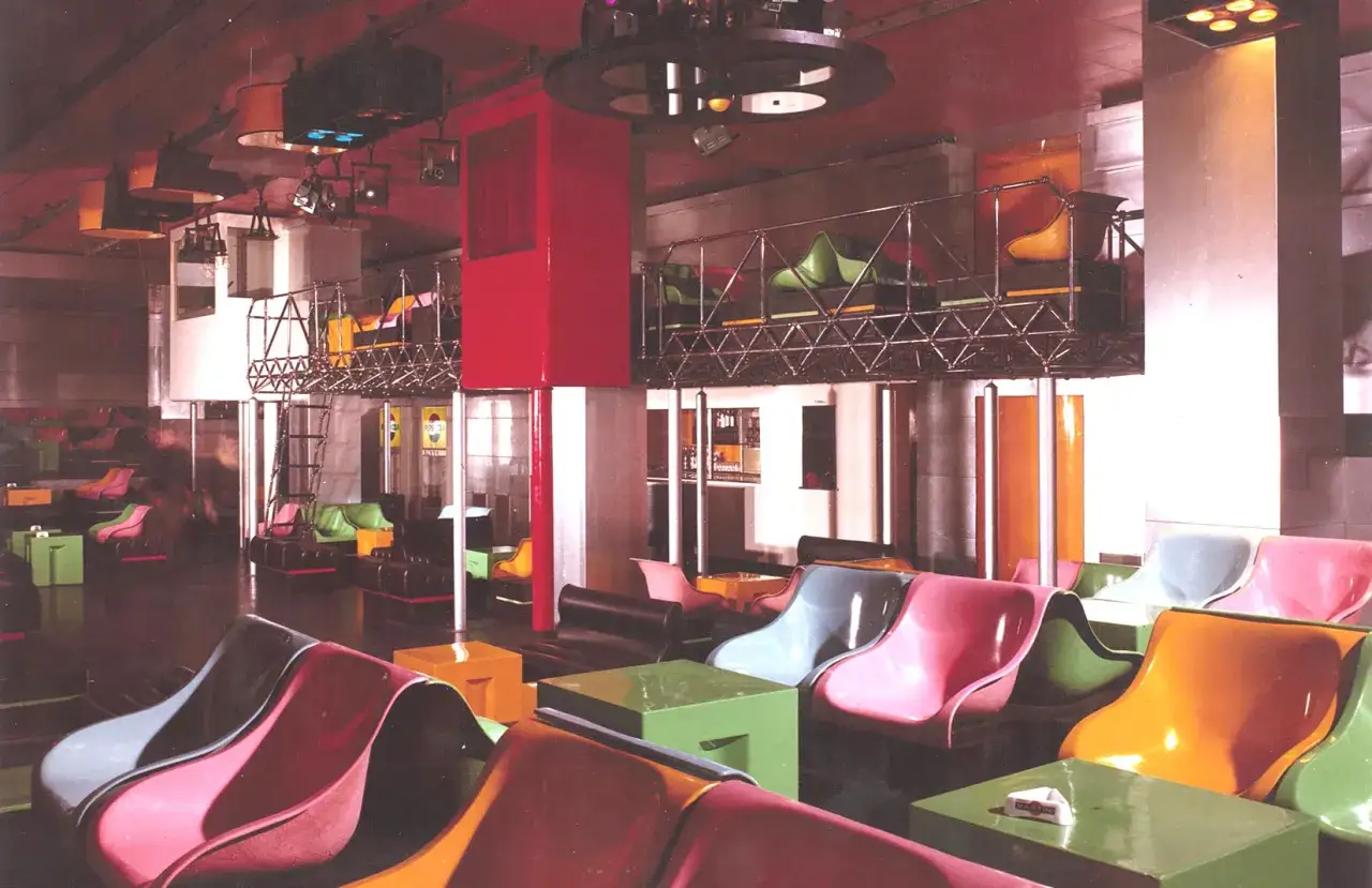 Kolorowe fotele i stoliki w klubie, przypominające wnętrza legendarnego Studio 54.