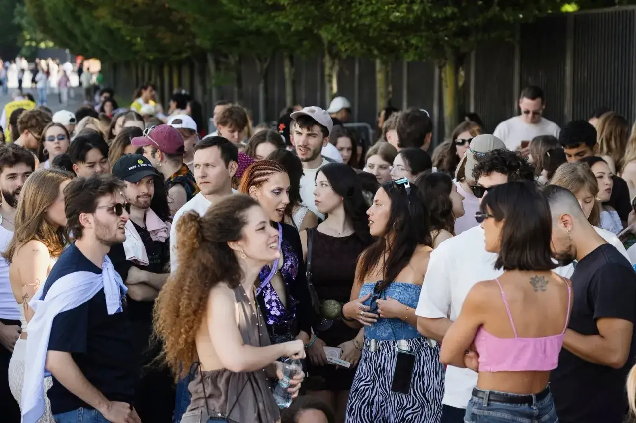Tłum ludzi czeka na koncert PGE Narodowy. Wszyscy podekscytowani, w letnich strojach, rozmawiają i cieszą się atmosferą.
